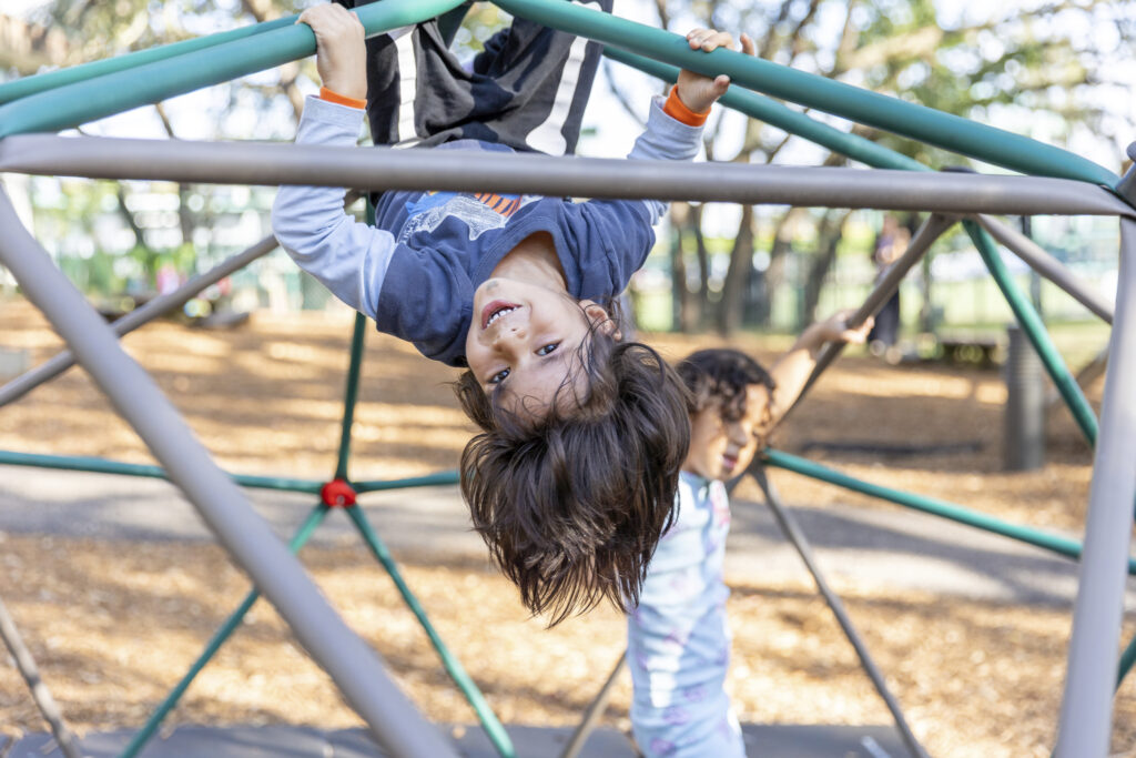 Two preschool children laughing while playing on a dome climber at the Preschool for Creative Learning